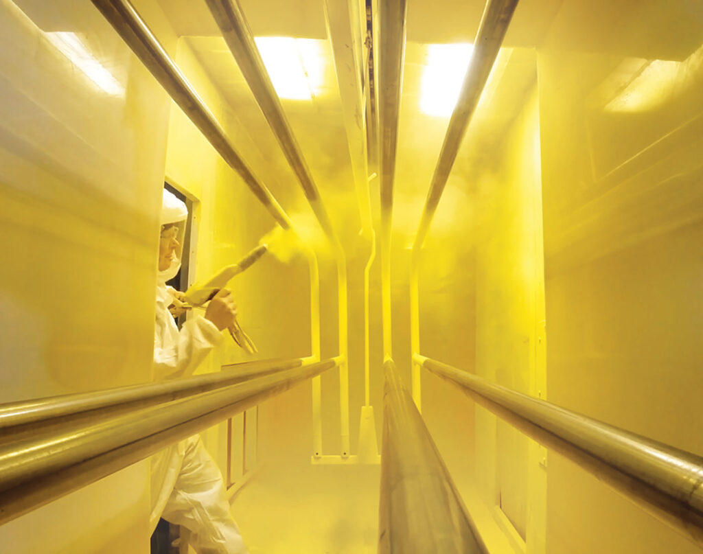 man painting rail in paint booth